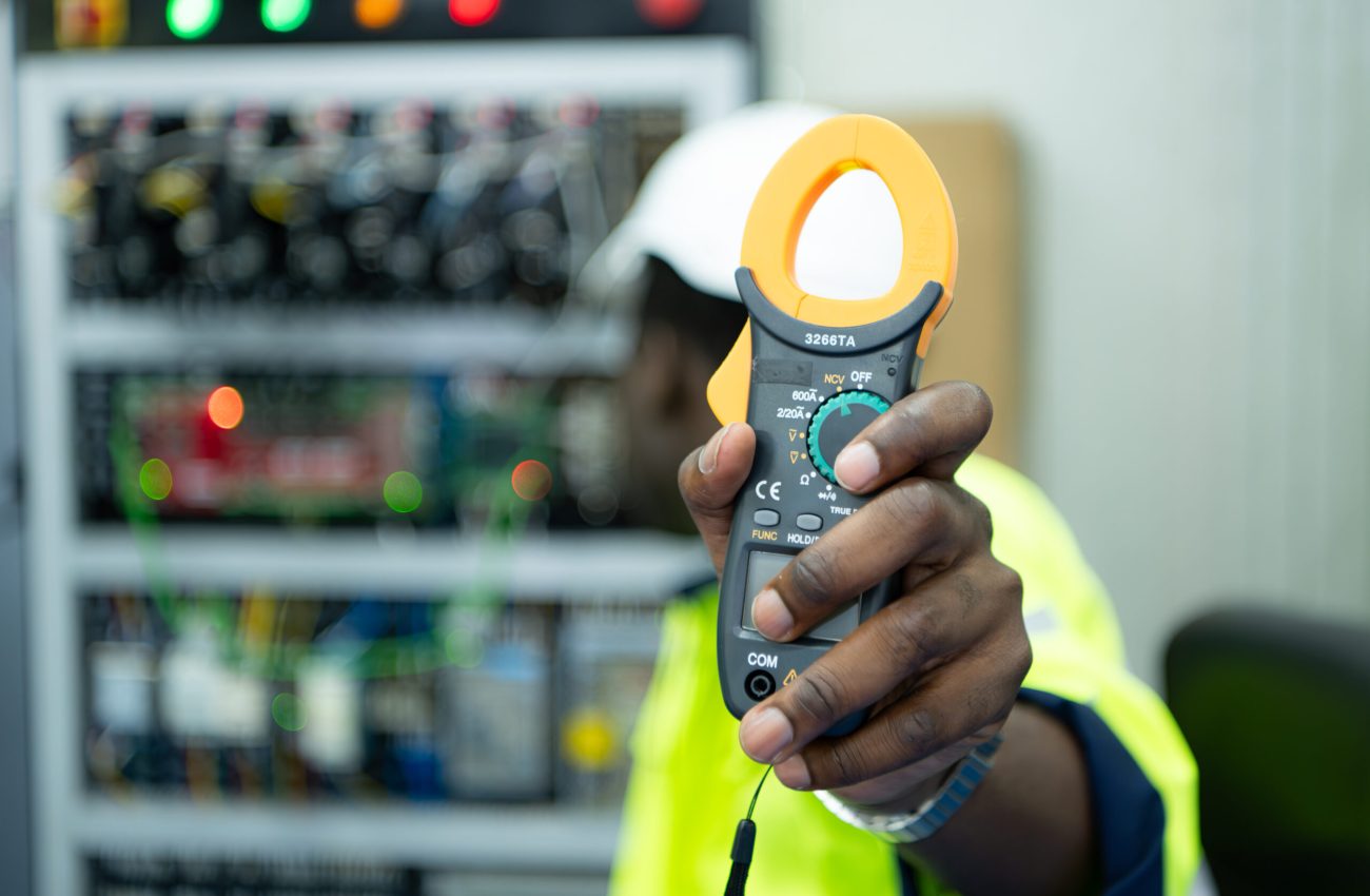 Portrait of a technician working with a digital multimeter to test the electrical system of a huge circuit board at an industrial plant using an automated hand robot.